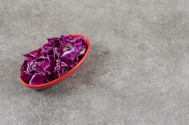 Foto gratuita una ciotola piena di mucchio di cavolo rosso tagliato su un tavolo di pietra.