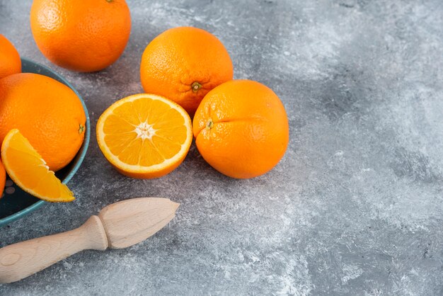 A bowl full of sliced and whole juicy orange fruits with wooden reamer .