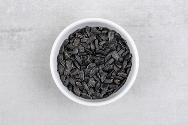 Bowl full of sunflower black seeds placed on stone table . 