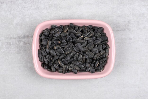 Bowl full of sunflower black seeds placed on stone table . 