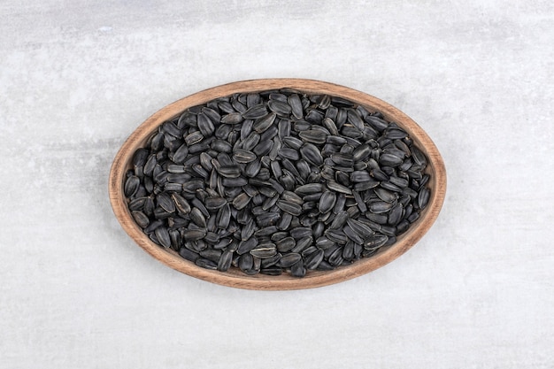 Bowl full of sunflower black seeds placed on stone .