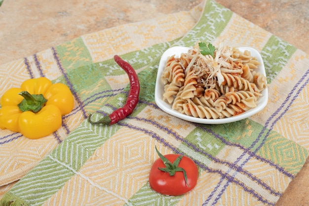 Bowl of fusilli pasta and fresh vegetables on tablecloth