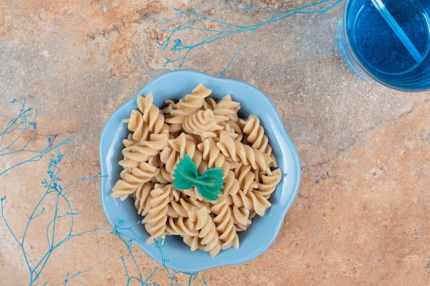 Bowl of fusilli pasta and glass of blue cocktail on marble background