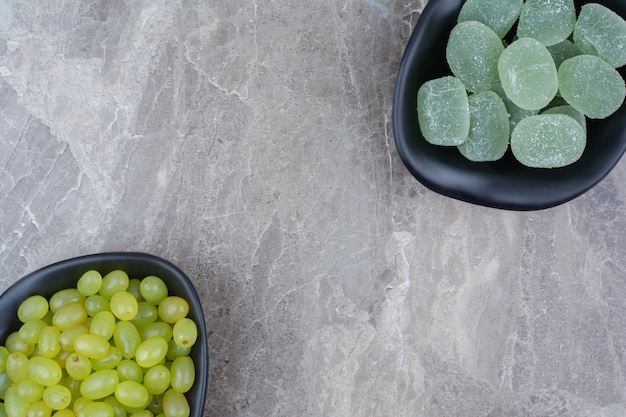 Bowl of grapes and marmalade candies on stone background. 