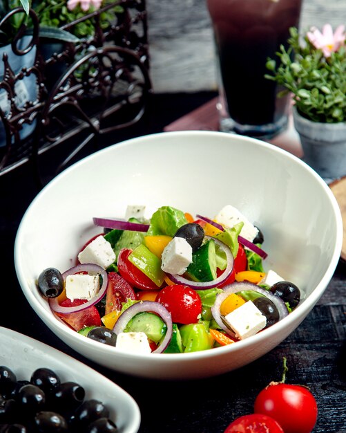 A bowl of greek salad with cucumber tomato yellow pepper red onion olive and white cheese