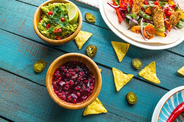 Bowl of guacamole with vegan salad on a pita and chips on a blue wooden table under the lights