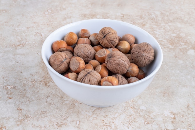 Foto gratuita una ciotola di nocciole e noci in una ciotola, sul tavolo di marmo