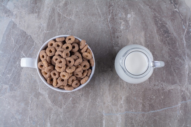 A bowl of healthy chocolate cereal rings with a glass jar of milk.