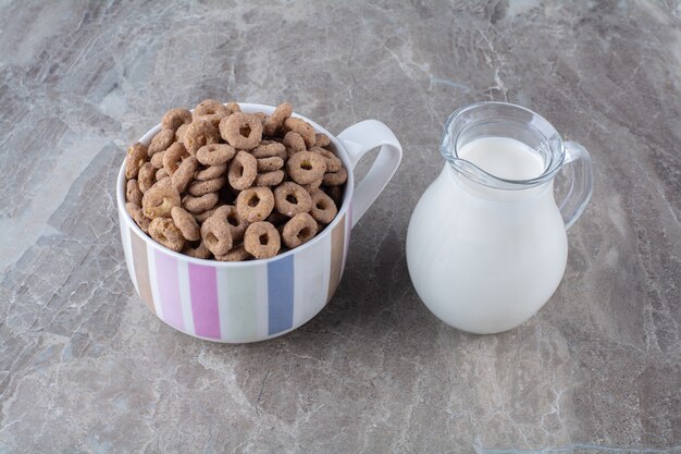 A bowl of healthy chocolate cereal rings with a glass jar of milk.