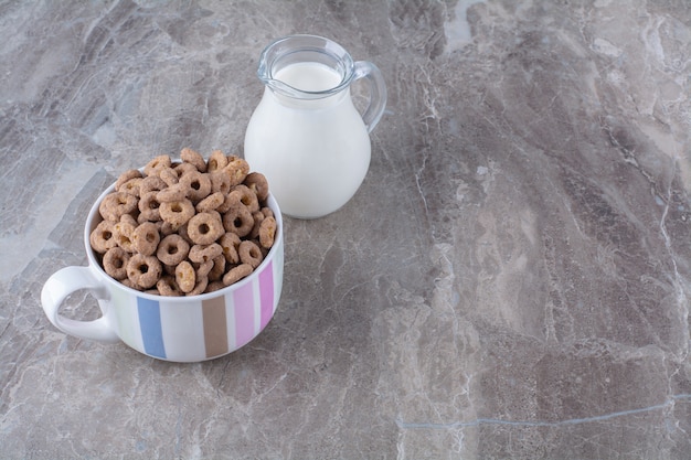 A bowl of healthy chocolate cereal rings with a glass jar of milk.