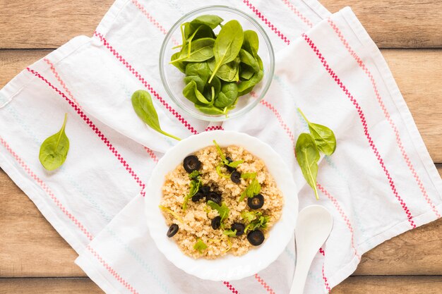 Bowl of healthy oats garnished with basil leaf and olive in bowl over cloth