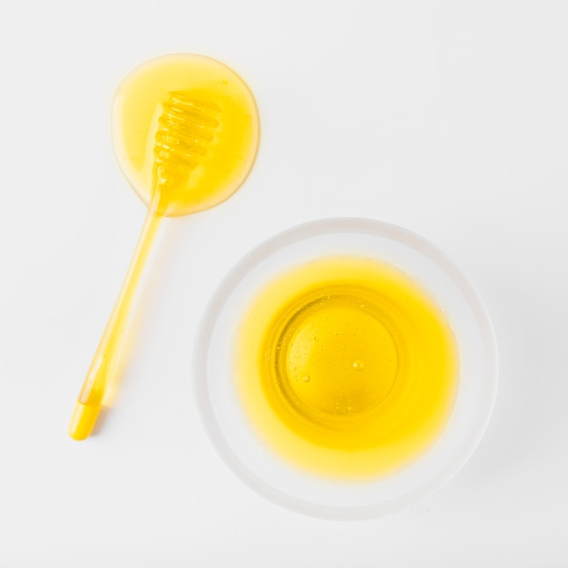 Bowl of honey and dipper on white surface