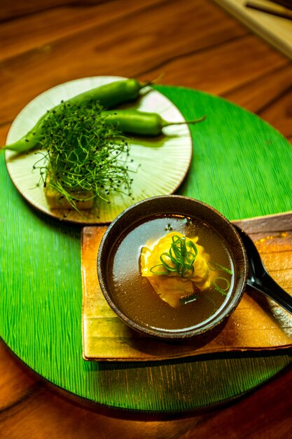 A bowl of japanese soup and a plate of green pepper and herbs