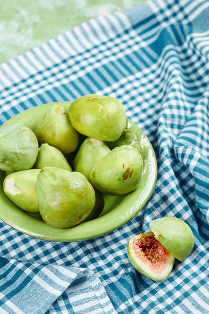 A bowl of juicy green figs and slices of fig on blue tablecloth.