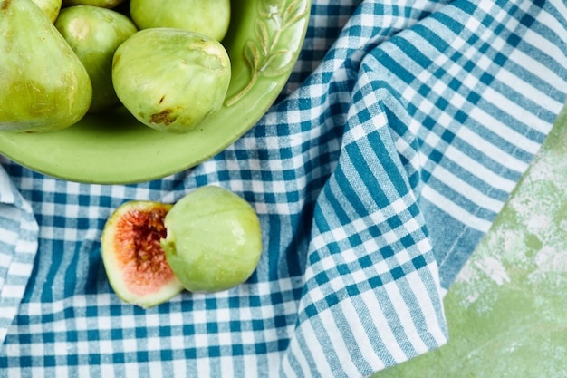 Free photo a bowl of juicy green figs and slices of fig on blue tablecloth.