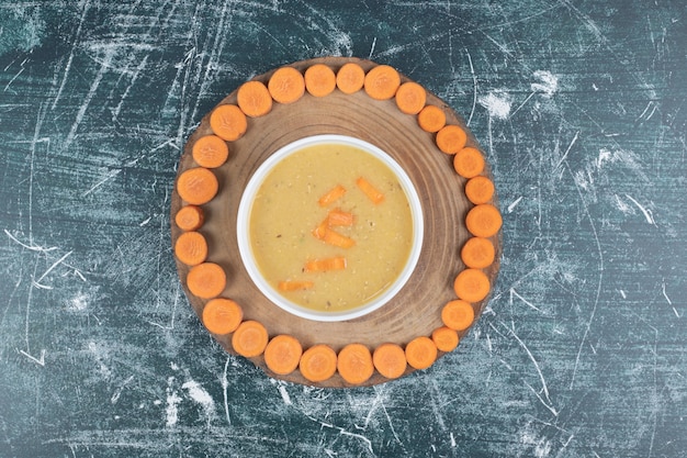 Free photo bowl of lentil soup and carrot slices on wooden plate.