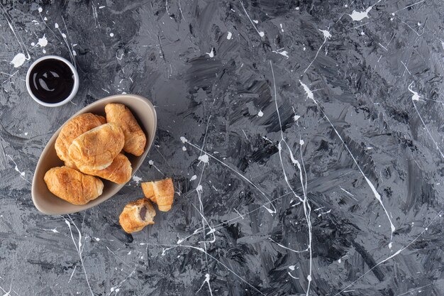 A bowl of mini croissants with chocolate placed on a marble background. 