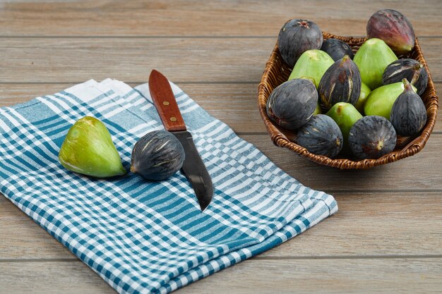 A bowl of mixed figs on wooden table with a knife and a tablecloth.