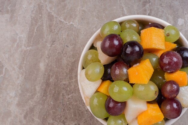 Bowl of mixed fruits on marble surface.