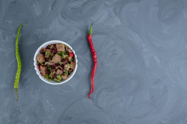 Free photo bowl of mixed salad in the middle of two peppers on marble table.