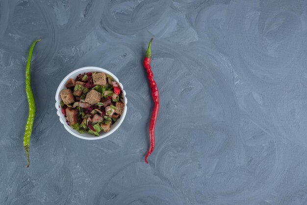 Bowl of mixed salad in the middle of two peppers on marble table.