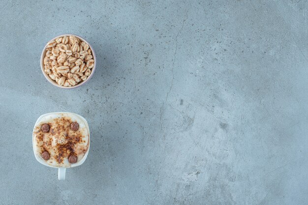A bowl of muesli and a cup of cappuccino, on the blue background.