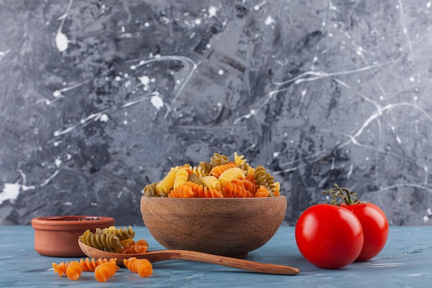 Free photo a bowl of multi colored raw spiral pasta with fresh red tomatoes and spices.