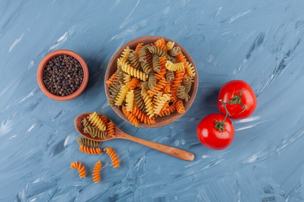 A bowl of multi colored raw spiral pasta with fresh red tomatoes and spices.