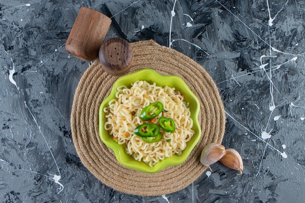 Bowl of noodle with pepper on a trivet, on the marble surface