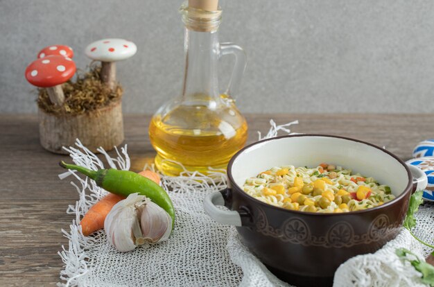 Bowl of noodles, bottle of oil and vegetables on wooden table