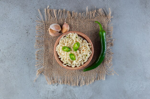 Миска лапши рядом с перцем и чесноком на мешковине, на мраморном фоне.