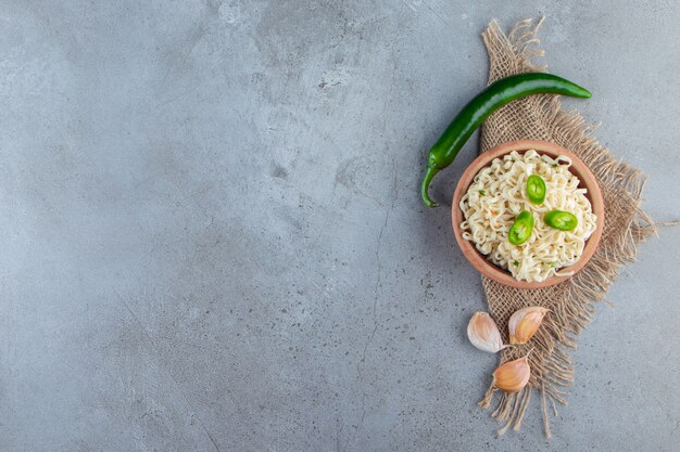 大理石の背景に、黄麻布のコショウとニンニクの横にある麺のボウル。