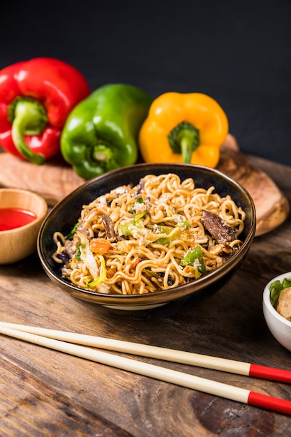 Bowl of noodles with bell peppers and chopstick on wooden desk