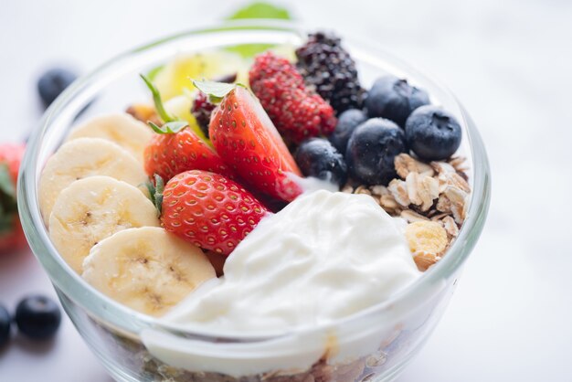 Bowl of oat granola with yogurt, fresh blueberries, mulberry, strawberries, kiwi, banana, mint and nuts board for healthy breakfast, top view, copy space, flat lay. vegetarian food concept.