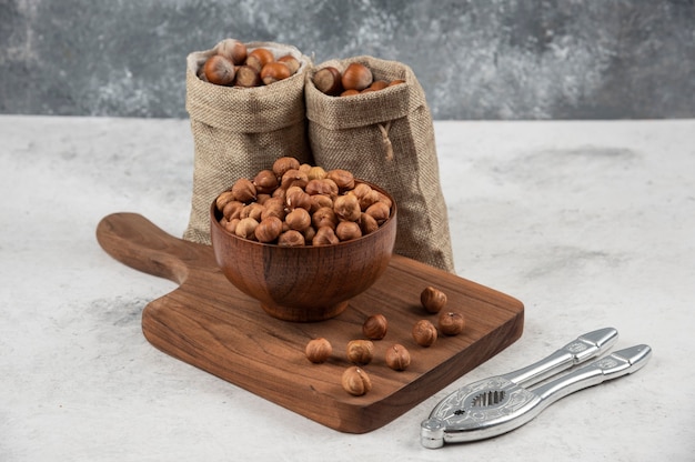 Bowl of organic hazelnut kernels on cutting board with shelled hazelnuts. 