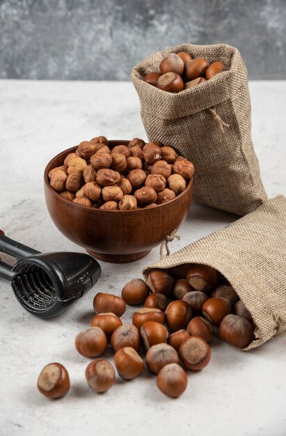 Bowl of organic hazelnut kernels and shelled hazelnuts on marble table. 