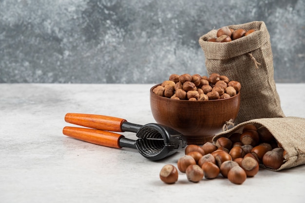 Bowl of organic hazelnut kernels and shelled hazelnuts on marble table. 