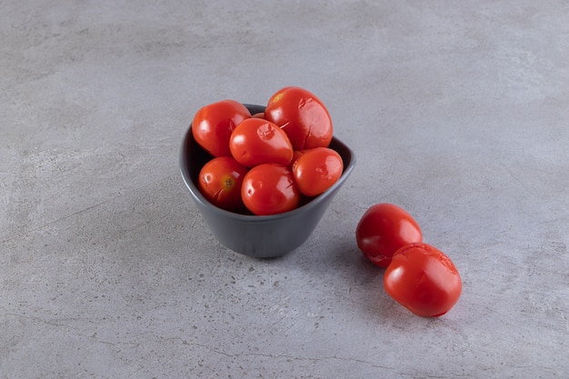 Bowl of pickled tomatoes placed on stone surface.