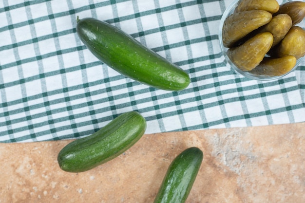 Bowl of pickles and fresh cucumbers on tablecloth.