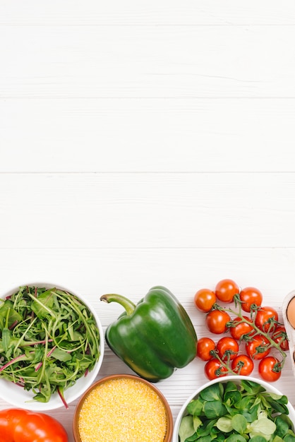 Ciotola di polenta e verdure a foglia sulla scrivania in legno bianco