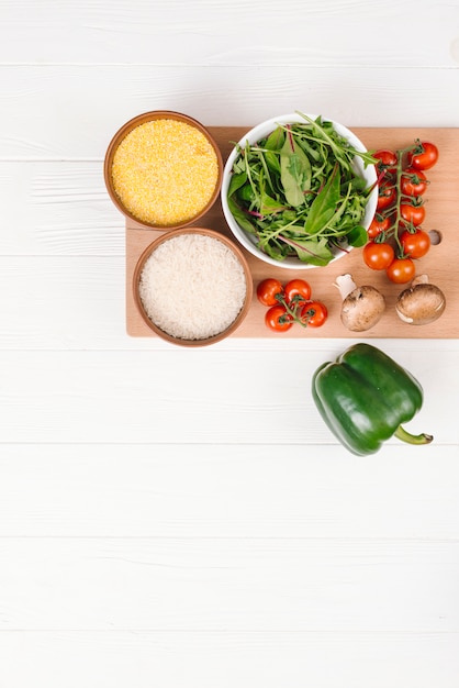 Free photo bowl of polenta; rice grains; leafy vegetables; mushroom; cherry tomatoes and bell pepper on white plank