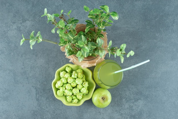 Bowl of popcorn candy, glass of apple juice, single apple and a wrapped wase with a decorative plant on marble background. High quality photo