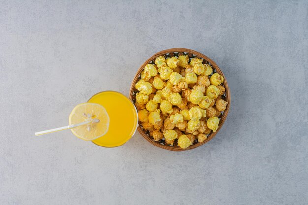 Bowl of popcorn candy and a glass of juice with a lemon slice on marble surface