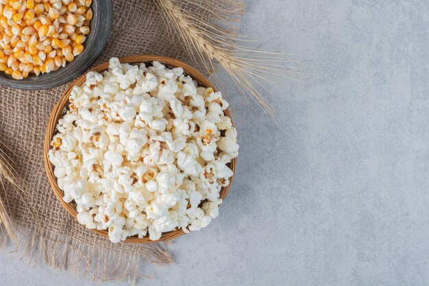 Bowl of popcorn, jug of corn and a wheat stalk on a piece of cloth on marble surface