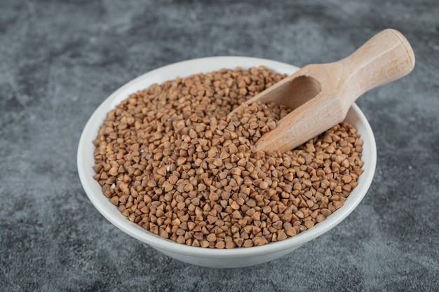 Bowl of raw buckwheat on marble surface