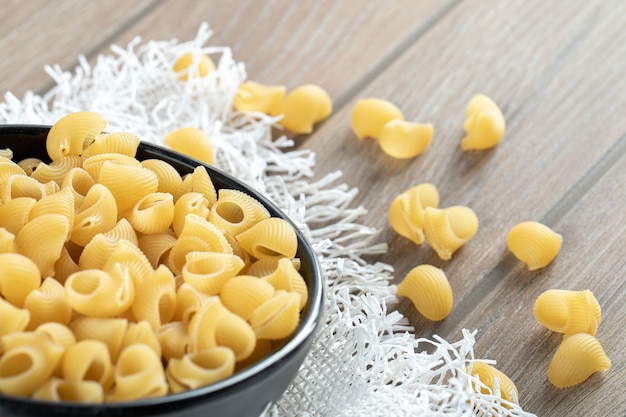 Bowl of raw dry seashell pasta placed on wooden surface