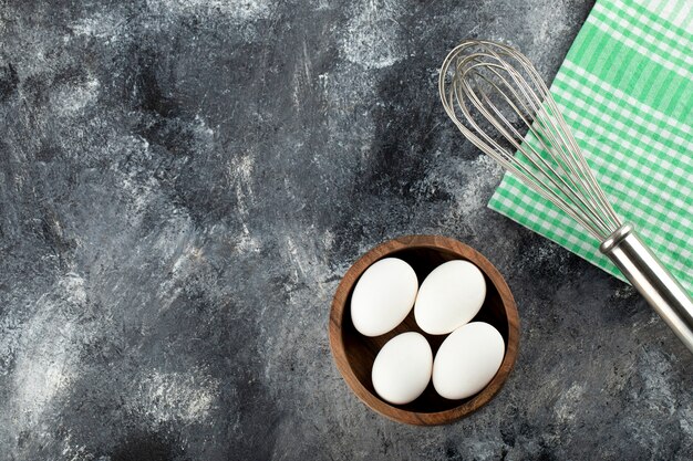 Bowl of raw eggs and whisker on marble surface. 