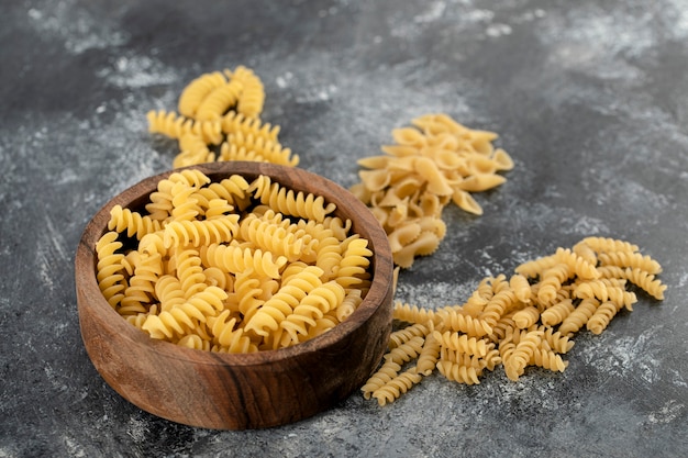 Bowl of raw fusilli pasta on marble surface