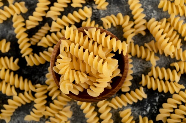 Bowl of raw fusilli pasta on marble surface