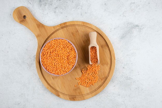 Bowl of raw lentils and spoon on cutting board.